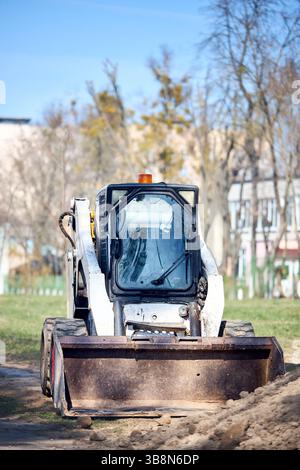 Miniescavatore bulldozer vecchio sporco e arrugginito vicino alla strada su sfondo urbano con messa a fuoco selettiva per fotogramma verticale frontale Foto Stock