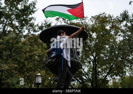 15 ottobre 2023, Washington, District of Columbia, USA: Un manifestante sventola la bandiera palestinese in cima a una fontana in Lafayette Square, Washington, District of Columbia, domenica 15 ottobre, 2023. la manifestazione faceva parte di uno sforzo globale per chiedere un cessate il fuoco immediato e duraturo a Gaza. (Immagine di credito: © Natascha Tahabsem/ZUMA Press Wire) Foto Stock