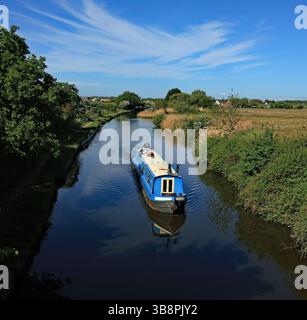Una barca blu sotto un grande cielo che viaggia verso Liverpool lungo il canale di Leeds e Liverpool a Halsall nel Lancashire occidentale. Foto Stock