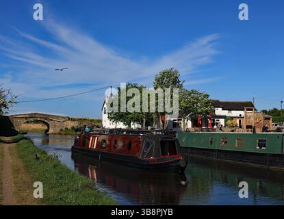 Un battello ristretto Maroon passa davanti al Saracens Head Pub sotto un grande cielo blu sopra il canale di Leeds e Liverpool a Halsall nel Lancashire occidentale. Foto Stock