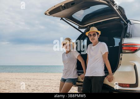 Una coppia asiatica sta posato sul retro di un'auto e gode di una splendida vista sulla spiaggia dell'oceano. uomo di stile di vita Foto Stock