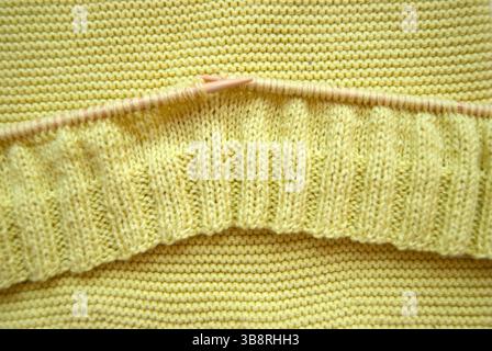 Maglia con aghi di legno. Un primo piano di tessuto giallo lavorato a maglia. Maglione lavorato a maglia. Foto Stock