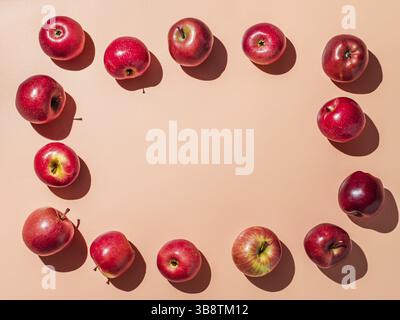 Mele rosse su sfondo arancione o rosa corallo con spazio per il testo o il disegno al centro, cornice di frutta colorata. Concetto creativo. Posa piatta o superiore vi Foto Stock