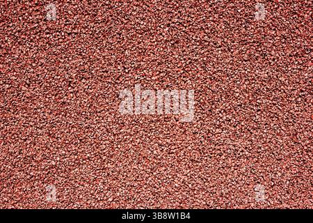Superficie granulosa rossa. Primo piano sulla struttura della pista da corsa. Materiale in gomma ruvida con effetto rumore. Sfondo sportivo. Dettagli sul campo sportivo. Terreno resistente Foto Stock
