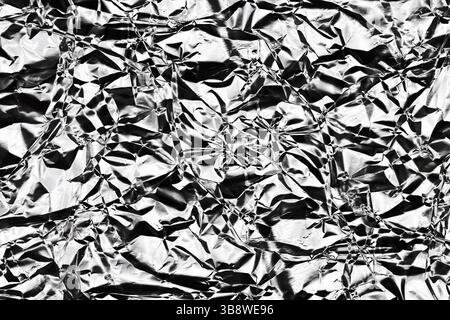Lamina spiegazzata. Superficie in argento lucido con pieghe metalliche. Sfondo deformato con riflessi di luce. Primo piano del materiale di imballaggio. Foto Stock