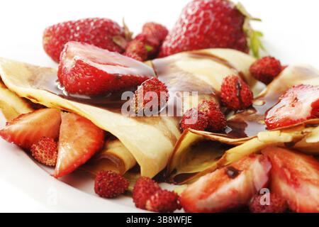 Frittelle con differenti le fragole con lo sciroppo di cioccolato su bianco Foto Stock