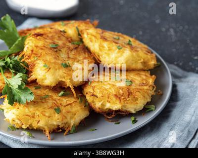 Vista ravvicinata delle frittelle di patate. Patate frittelle latkes, flapjacks, hashbrown o patate vada su piatto grigio su tavolo di legno grigio, con pars freschi Foto Stock