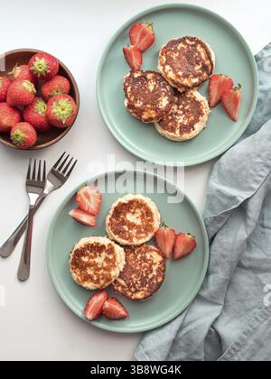 Frittelle dolci al formaggio sul piatto servite con fragole. Frittelle di formaggio, sciroppi, frittelle di ricotta, frittelle di cagliata. Vista dall'alto o disposizione piatta. Verticale Foto Stock