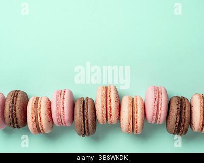 Macarons con spazio di copia. Fila di macaron francesi perfetti o macaron su sfondo blu turchese. Vista dall'alto o piatto Foto Stock
