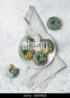 Ciambelle vegane con semi di chia ricoperti di sana glassa spirulina con pistacchio, cocco essiccato e mirtillo. Ciambelle con spirulina verde blu su g Foto Stock