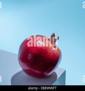 Melograno art. Fresco granato maturo su piedistallo blu pastello su sfondo blu in luce dura. Scatto creativo di melograno. Design creativo con Foto Stock