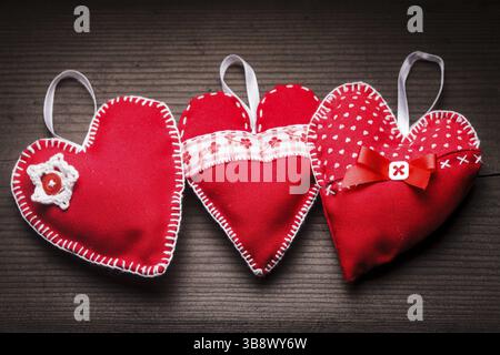 Cucite a mano cuori rossi su sfondo di legno Foto Stock