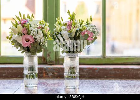 Due splendidi bouquet nuziali con fiori rosa e bianchi poggiati su una davanzale in vasi di vetro decorati Foto Stock