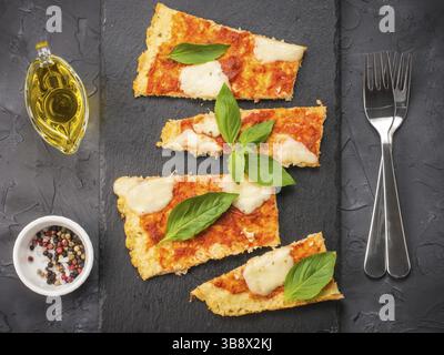 Vista dall'alto della crosta di pizza fatta in casa con cavolfiore a fette con mozarella e basilico fresco su un piatto di ardesia su sfondo nero di cemento Foto Stock