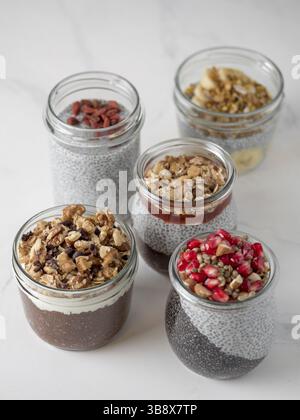 Set di budino di chia in diversi vasetti di vetro su marmo bianco. Assortimento di chia puding con frutta e noci diverse. Copia spazio per il testo. S Foto Stock