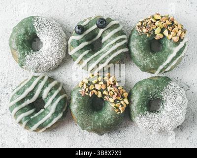 Vegan ciambelle con semi di Chia e rabboccato con sani spirulina smalto con pistacchio, noce di cocco essicata e mirtillo. Blu Verde spirulina ciambelle, su Foto Stock