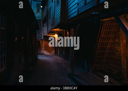 Suggestive scene notturne da Bryggen Wharf a Bergen, Norvegia, che mostrano negozi accoglienti, vicoli illuminati ed edifici storici in legno in caldi luci Foto Stock