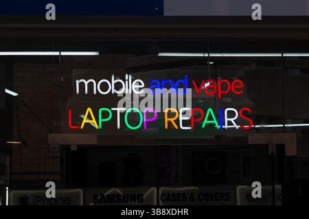 Un cartello al neon su un negozio che pubblicizza la riparazione di telefoni cellulari, vapes e laptop. Cambridge, Inghilterra, Regno Unito Foto Stock