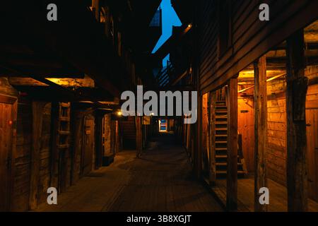 Suggestive scene notturne da Bryggen Wharf a Bergen, Norvegia, che mostrano negozi accoglienti, vicoli illuminati ed edifici storici in legno in caldi luci Foto Stock