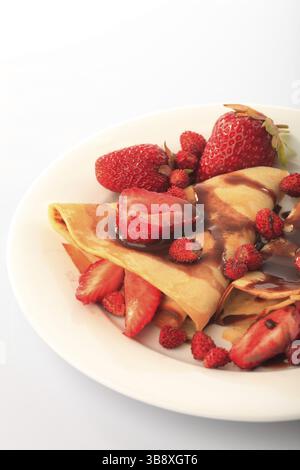 Frittelle con differenti le fragole con lo sciroppo di cioccolato su bianco Foto Stock