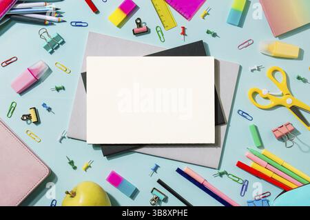 Scrivania creativa per studenti con foglio bianco di carta per notebook e materiale per la scuola. Vista dall'alto con spazio per la copia. Torna a scuola appartamento su sfondo blu e rosa Foto Stock
