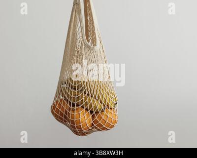 Sacchetto in rete con frutta in mano femminile. Borsa della spesa in rete da donna tenuta a mano su una parete grigio chiaro. Shopping moderno e riutilizzabile, concetto di zero rifiuti Foto Stock