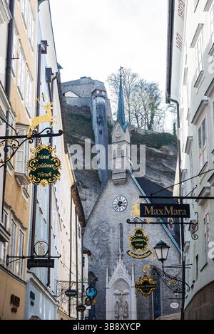 Salisburgo, Austria - 2 aprile 2025: Getreidegasse, negozi e chiesa di San Blasio nella città vecchia di Salisburgo, Austria Foto Stock