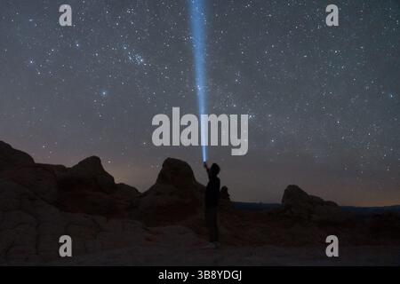 Silhouette di un uomo che regge una torcia blu al cielo notturno. Nel profondo del deserto di White Pocket nel monumento nazionale di Vermillion Cliffs Foto Stock