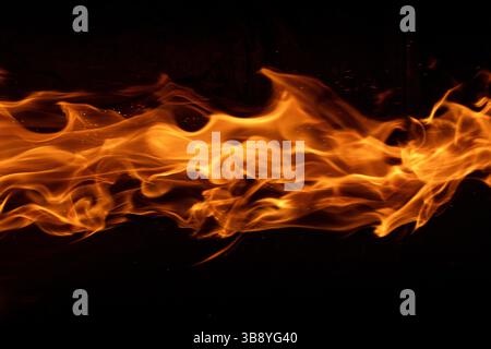 Le fiamme danzanti si estendono orizzontalmente su uno sfondo nero profondo, catturando la natura ipnotica ed eterea del fuoco in movimento. Foto Stock