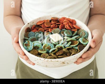 Cibo alla moda - pancake e cereali. Mini frittelle di cereali colorate in ciotola nelle mani dei bambini. Il bambino tiene in mano minuscole frittelle con colorante naturale: Matcha verde, tacca di tacca Foto Stock