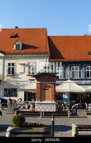 Un accogliente caffè all'aperto con gente che si gode una giornata di sole, ombreggiato da ombrelloni, accoccolato tra affascinanti edifici in stile europeo con tetti di tegole rosse Foto Stock