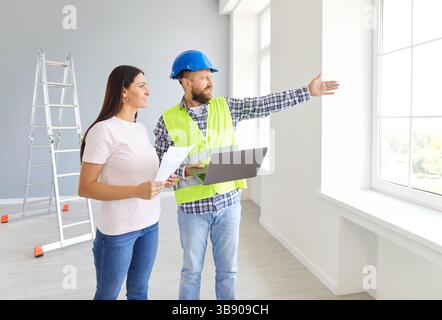 Ingegnere edile professionista e proprietaria di una casa che guarda fuori dalla finestra e parla Foto Stock