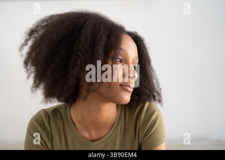 Giovane donna premurosa con capelli ricci naturali che si guardano da parte nella luce soffusa del giorno. Concetti di bellezza, identità e diversità. Foto Stock