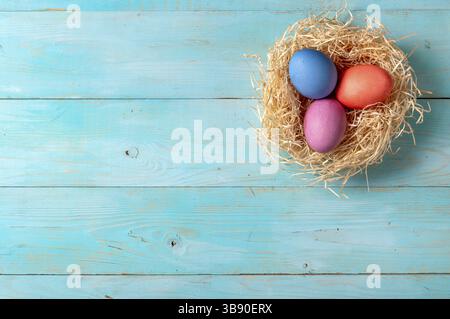 Concetto di Pasqua. Uova colorate su sfondo di legno blu con spazio di copia per il testo. Vista dall'alto verso il basso o piatto Foto Stock