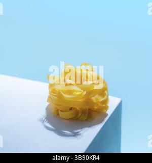 Pasta art. Tagliatelle su piedistallo blu pastello su sfondo blu in luce dura. Un tocco creativo di pasta noodle. Design creativo per menu di ital Foto Stock