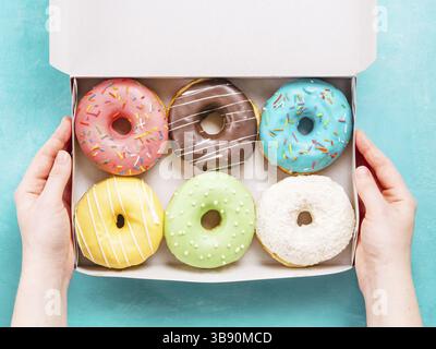 Vista dall'alto di mani femminili della scatola di contenimento con ciambelle colorate in blu sullo sfondo di calcestruzzo Foto Stock