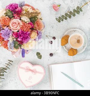 Lay piatto con bel bouquet, tazza di caffè, confezione regalo a forma di cuore, notebook vuota per la scrittura di sogni e di idee. Vista dall'alto. Formato quadrato. Un concetto Foto Stock