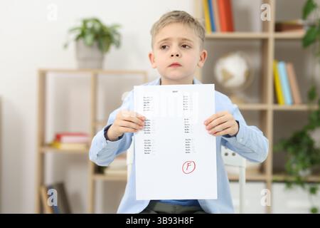 Grado scolastico. Ragazzo triste che tiene in mano il foglio delle risposte con la lettera F in casa Foto Stock