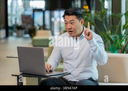 Eureka. Un uomo d'affari cinese attento e intelligente che utilizza il laptop fa alzare il dito con un piano creativo si sente entusiasta di una domanda motivazionale di ispirazione per una buona idea nella hall dell'hotel. Foto Stock