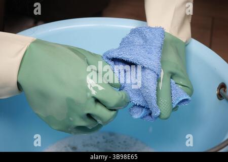 Processo di pulizia in corso con guanti verdi e un panno blu Foto Stock
