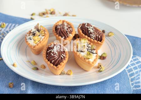 Tartarughe di impasto sabbiate con ripieno di cioccolato, pistacchio su piatto bianco. Dessert per la festa, per le vacanze. Foto Stock