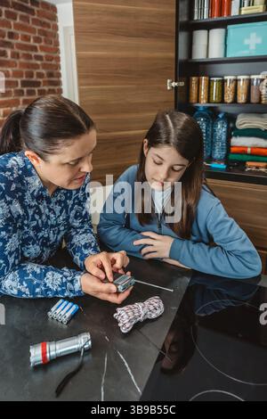 Madre e figlia ascoltano notizie di emergenza in un piccolo ricevitore radio portatile durante il blackout elettrico. Famiglia pronta con dispensa alimentare di emergenza in k Foto Stock
