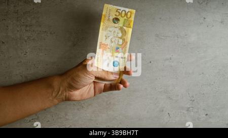 Uomo in possesso di banconota da 500 peso delle filippine su sfondo concreto Foto Stock