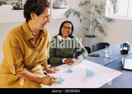 Due donne professionali che lavorano insieme a un progetto in una riunione collaborativa in un ufficio moderno. Questa immagine riflette leadership, lavoro di squadra e posi Foto Stock