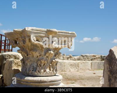 Un'antica capitale di colonne di pietra splendidamente dettagliata situata tra le rovine di un sito storico, impreziosita da un cielo azzurro luminoso e da nuvole sparse Foto Stock