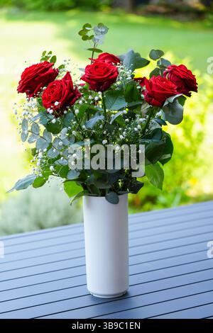Un bouquet di rose rosse in un vaso bianco sul tavolo da giardino Foto Stock