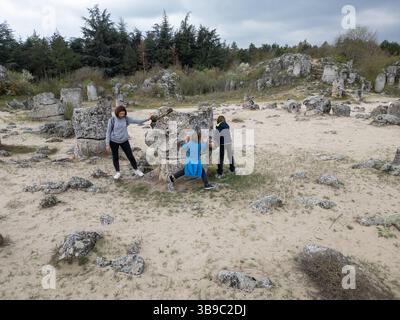 Madre e due bambini esplorano il terreno roccioso in un paesaggio arido e semi-desertico. I bambini giocano su formazioni di pietra mentre la madre guarda, enjo Foto Stock