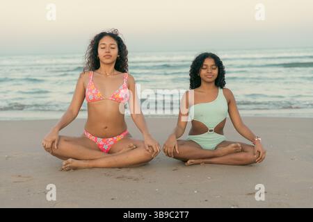 Due donne che meditano su una spiaggia tranquilla Foto Stock