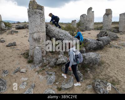 Madre e due bambini esplorano il terreno roccioso in un paesaggio arido e semi-desertico. I bambini giocano su formazioni di pietra mentre la madre guarda, enjo Foto Stock