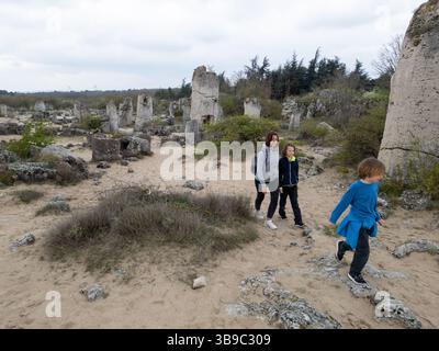 Madre e due bambini esplorano il terreno roccioso in un paesaggio arido e semi-desertico. I bambini giocano su formazioni di pietra mentre la madre guarda, enjo Foto Stock